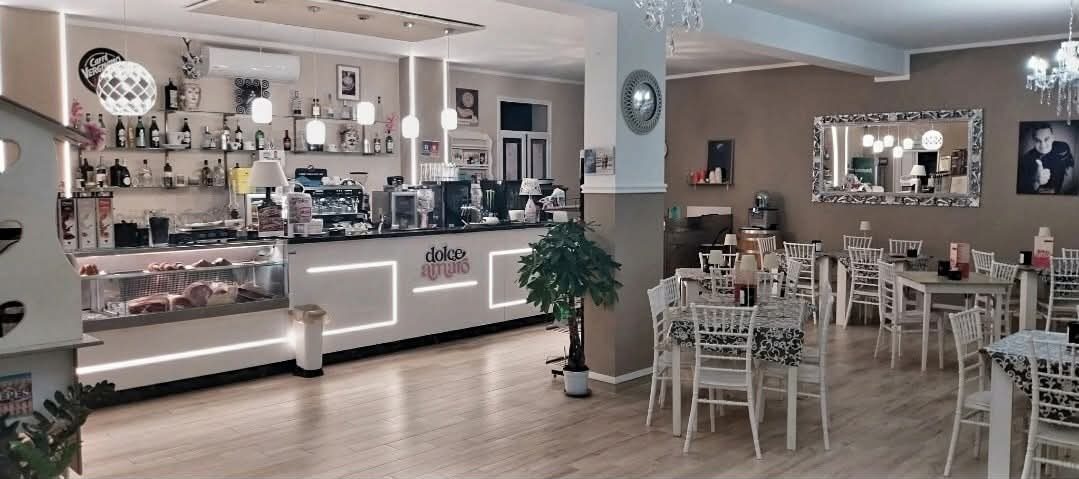 La sala di Dolce Amaro di sera: il bancone bianco con le luci a LED accese, i lampadari, lo specchio e i tavolini con le sedie bianche